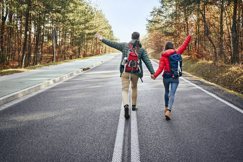 Happy couple walking in middle of an empty road in the woods - BSZF00908