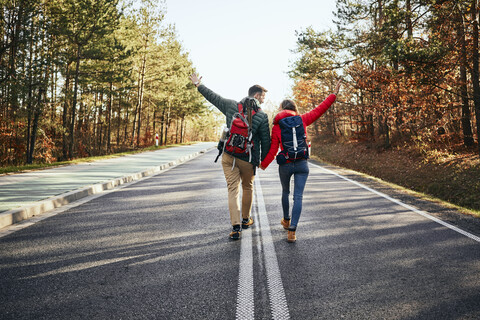 Glückliches Paar, das mitten auf einer leeren Straße im Wald spazieren geht, lizenzfreies Stockfoto