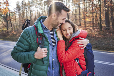 Happy couple embracing on a road in the woods during backpacking trip - BSZF00915