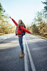 Happy woman standing in middle of an empty road during backpacking trip - BSZF00918