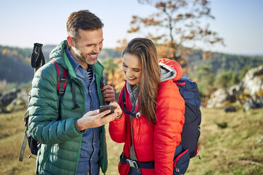 Glückliches Paar auf einer Wanderung in den Bergen, das sein Handy überprüft - BSZF00921