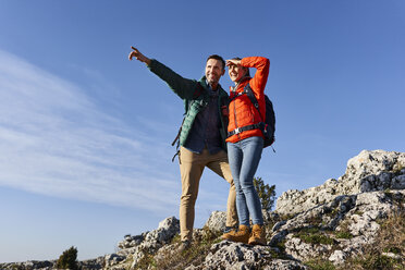 Happy couple on a hiking trip in the mountains standing on rock enjoying the view - BSZF00933