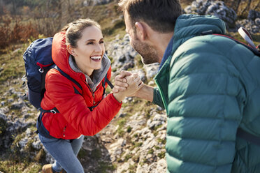 Man helping girlfriend climbing rock on a hiking trip in the mountains - BSZF00936