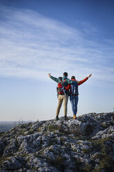 Happy couple on a hiking trip in the mountains standing on rock enjoying the view - BSZF00937