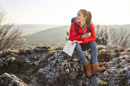 Frau beim Wandern in den Bergen, die auf einem Felsen sitzt und eine Pause macht - BSZF00941