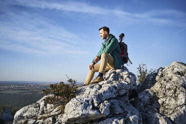 Mann auf einer Wanderung in den Bergen, der auf einem Felsen sitzt und die Aussicht genießt - BSZF00945