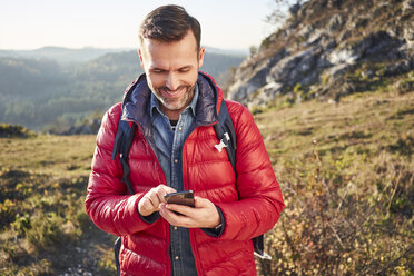 Lächelnder Mann bei einer Wanderung in den Bergen, der sein Handy überprüft - BSZF00957