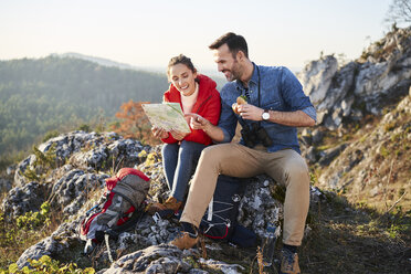 Happy couple on a hiking trip in the mountains taking a break looking at map - BSZF00959