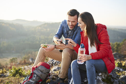 Glückliches Paar auf einem Wanderausflug in den Bergen, das eine Pause macht und auf sein Handy schaut - BSZF00960