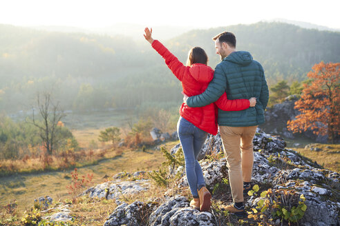 Rear view of happy couple on a hiking trip in the mountains standing on rock - BSZF00962