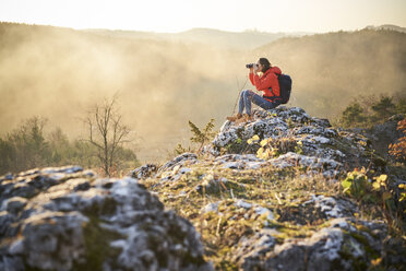 Woman on a hiking trip in the mountains sitting on rock looking through binoculars - BSZF00969