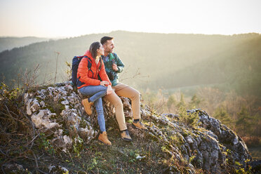 Pärchen beim Wandern in den Bergen, das auf einem Felsen sitzend eine Pause macht - BSZF00977