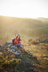 Couple on a hiking trip in the mountains having a break sitting on rock - BSZF00978