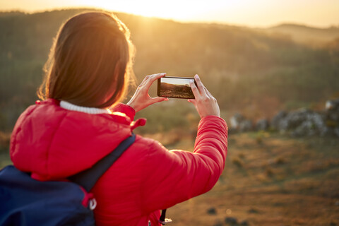 Frau auf einem Wanderausflug, die ein Smartphone-Foto bei Sonnenuntergang macht, lizenzfreies Stockfoto