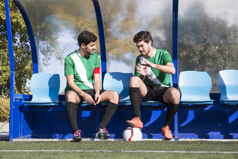 Zwei Fußballspieler sitzen auf einer Bank am Fußballplatz und unterhalten sich - ABZF02175