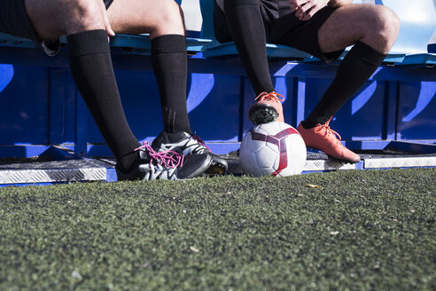 Beine von zwei Fußballspielern, die auf einer Bank am Fußballplatz sitzen - ABZF02178