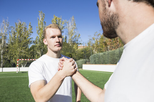 Two football players shaking hands on football field - ABZF02221
