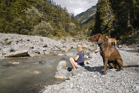 Österreich, Tirol, Mädchen mit zwei Hunden an einem Gebirgsbach, lizenzfreies Stockfoto