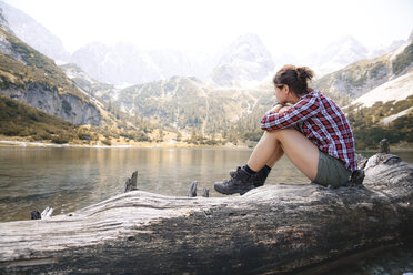 Austria, Tyrol, woman sitting on tree trunk at lake Seebensee - FKF03265