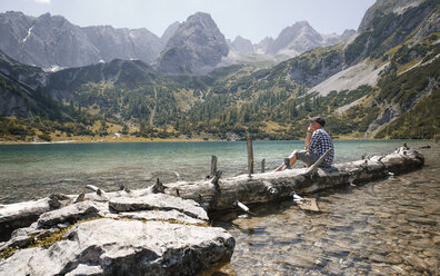 Österreich, Tirol, Mann sitzt auf Baumstamm am Seebensee - FKF03270