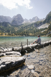 Austria, Tyrol, man sitting on tree trunk at lake Seebensee - FKF03271