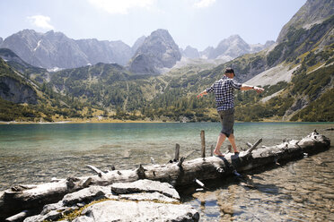 Austria, Tyrol, man balancing on tree trunk at lake Seebensee - FKF03272