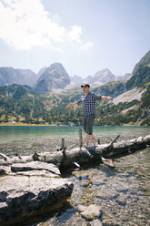 Austria, Tyrol, man balancing on tree trunk at lake Seebensee - FKF03273