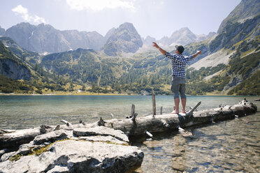 Austria, Tyrol, man standing on tree trunk at lake Seebensee - FKF03274