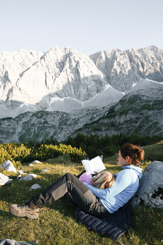 Österreich, Tirol, Mutter und Tochter lesen ein Buch in einer Berglandschaft, lizenzfreies Stockfoto