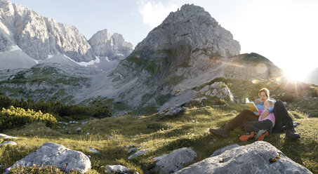 Österreich, Tirol, Mutter und Tochter lesen Buch in Berglandschaft bei Sonnenuntergang - FKF03287