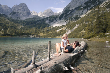 Austria, Tyrol, playful mother and daughter on tree trunk at lake Seebensee - FKF03289