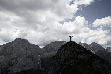 Austria, Tyrol, silhouette of man cheering on mountain peak - FKF03292