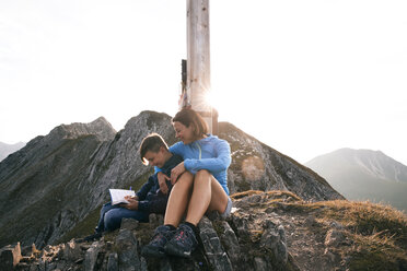 Österreich, Tirol, Mutter und Sohn beim Wandern mit Buch auf dem Gipfel - FKF03329