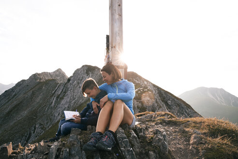 Österreich, Tirol, Mutter und Sohn beim Wandern mit Buch auf dem Gipfel - FKF03329