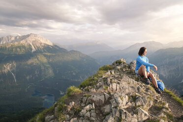 Austria, Tyrol, woman on a hiking trip in the mountains sitting on peak - FKF03332