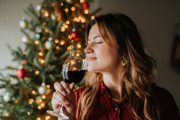 Frau riecht an einem Glas Wein neben einem geschmückten Weihnachtsbaum - ISF20784