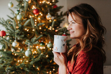 Frau trinkt Kaffee neben einem geschmückten Weihnachtsbaum - ISF20786