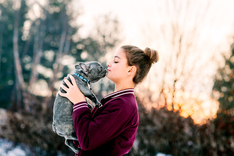 Mädchen küsst französische Bulldogge Welpe im Freien, lizenzfreies Stockfoto