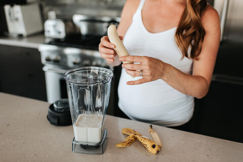 Schwangere Frau bereitet Smoothie in der Küche zu, lizenzfreies Stockfoto