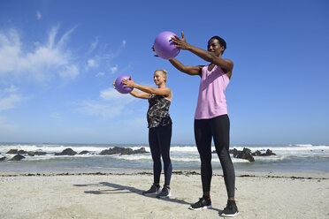 Zwei Frauen machen Fitnessübungen mit Ball am Strand - ECPF00463