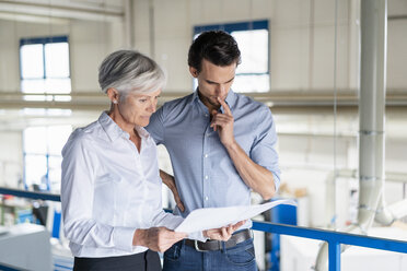 Businessman and senior businesswoman looking at plan in a factory - DIGF05729