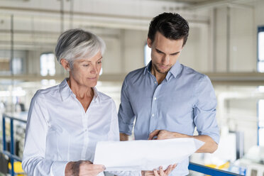 Businessman and senior businesswoman looking at plan in a factory - DIGF05730