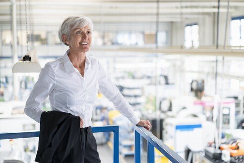 Lächelnde ältere Geschäftsfrau im oberen Stockwerk einer Fabrik mit Blick auf den Verkaufsraum - DIGF05731