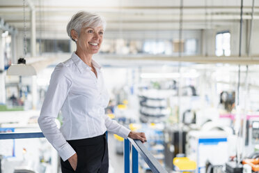 Smiling senior businesswoman on upper floor in factory overlooking shop floor - DIGF05732