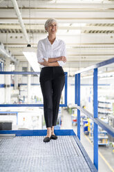 Confident senior businesswoman standing on upper floor in factory - DIGF05740