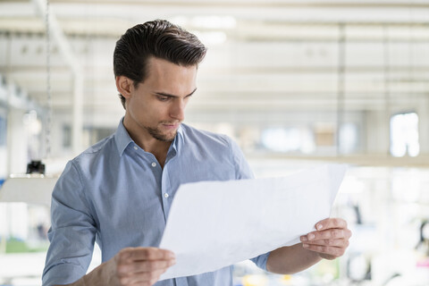 Geschäftsmann betrachtet einen Plan in einer Fabrik, lizenzfreies Stockfoto