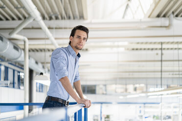 Businessman on upper floor in factory overlooking shop floor - DIGF05744