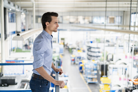 Geschäftsmann im Obergeschoss einer Fabrik mit Blick auf den Verkaufsraum, lizenzfreies Stockfoto