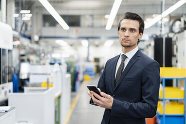 Portrait of businessman with cell phone in a factory - DIGF05754