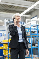 Lächelnde ältere Geschäftsfrau am Mobiltelefon in einer Fabrik - DIGF05764